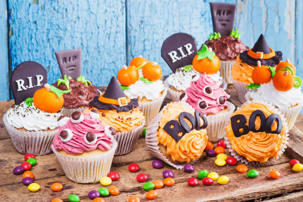 Halloween cupcakes with decorations: tombstone, eyes and pumpkins made from confectionery mastic, soft focus background