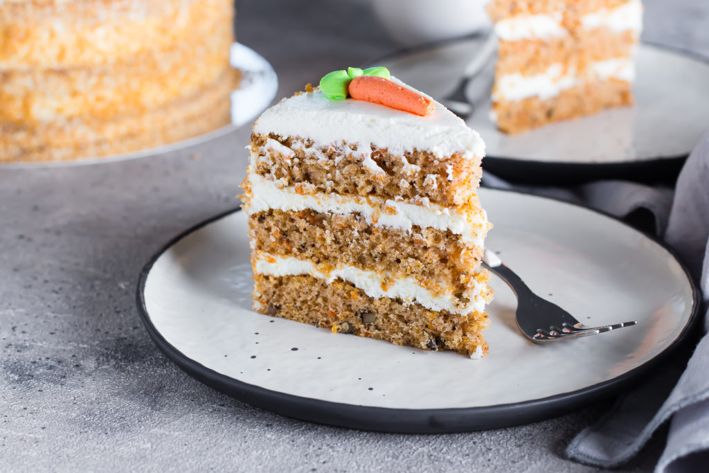 Slice of homemade carrot cake with cream cheese frosting on plate on gray stone table background