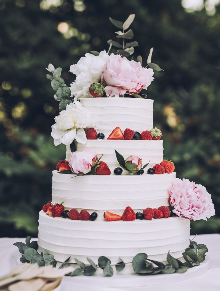 4 tier white wedding cake decorated with fresh fruit and fresh pink flowers